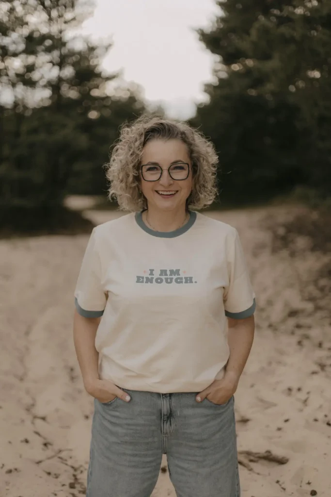 Uśmiechnięta właścicielka perfect space, zajmująca się declutteringiem i organizacją przestrzeni. Przyjazna kobieta w okularach w kręconymi blond włosami.